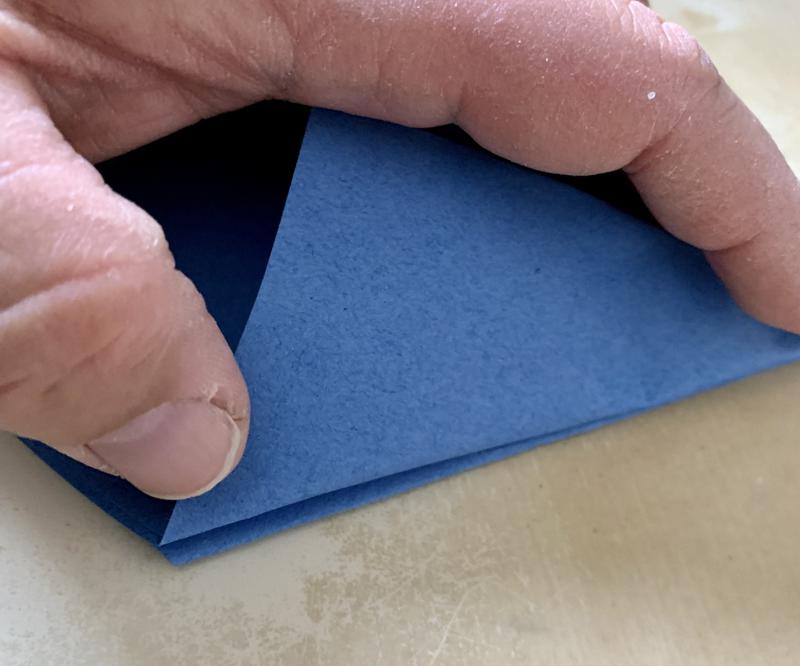 A thumb and index finger push the flap down so that its fold aligns with the fold of the other flap.