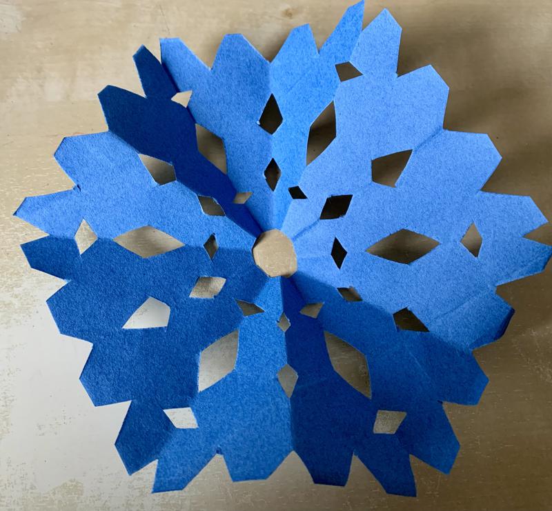 A hexagonal piece of blue paper with various holes cut into it, resembling a snowflake.